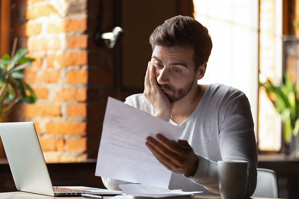 A frustrated young business owner reads loan paperwork with his head in his hands