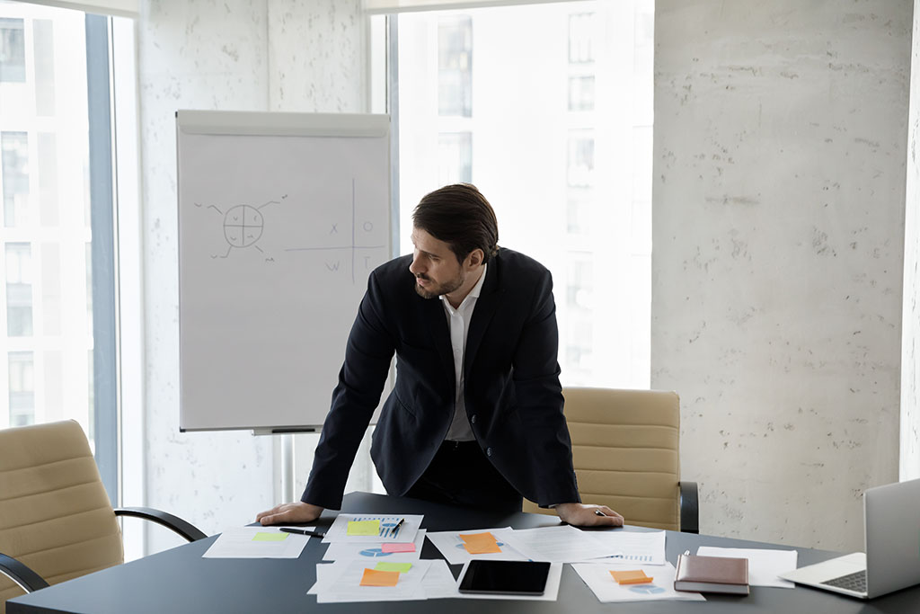 A frustrated small business owner stands in front of a paper-covered conference table