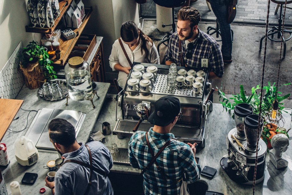 a group of people standing around a small business counter with coffee machines