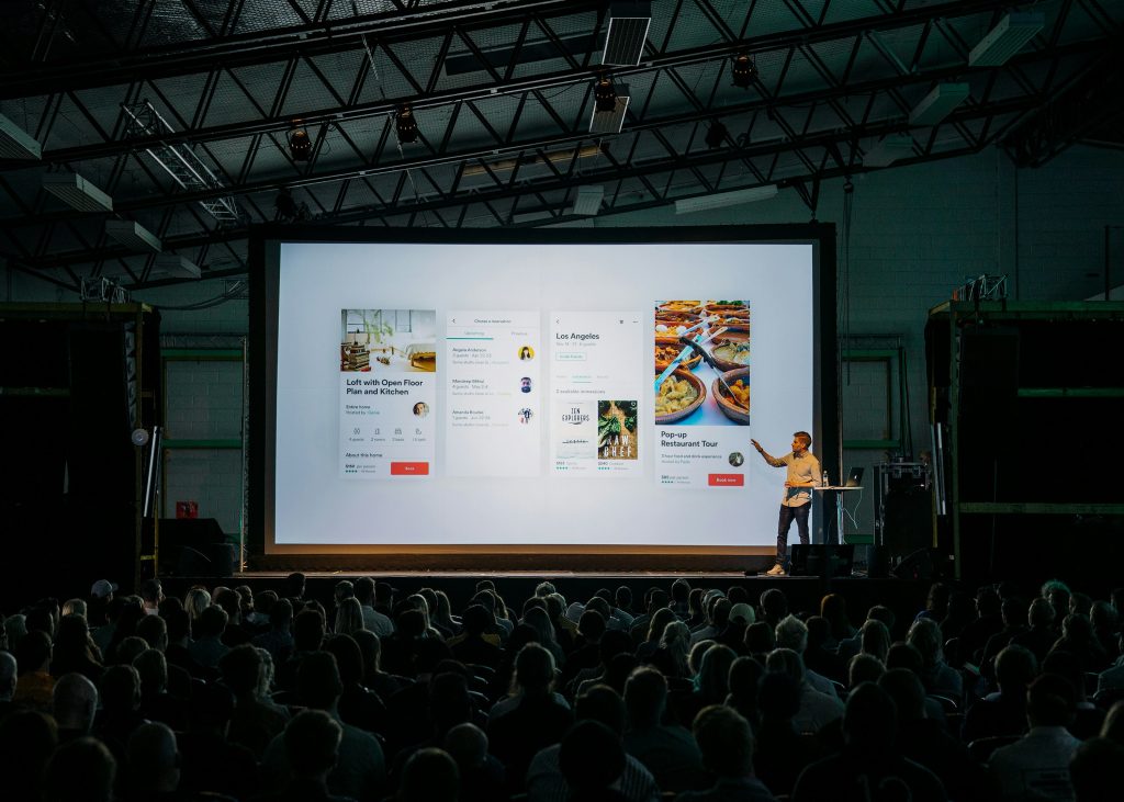 a man standing in front of a large screen with a large crowd watching similar to networking events in Atlanta