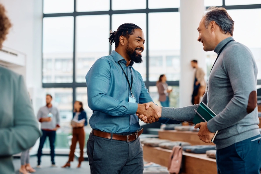 Two entrepreneurs shake hands and smile at a small business expo